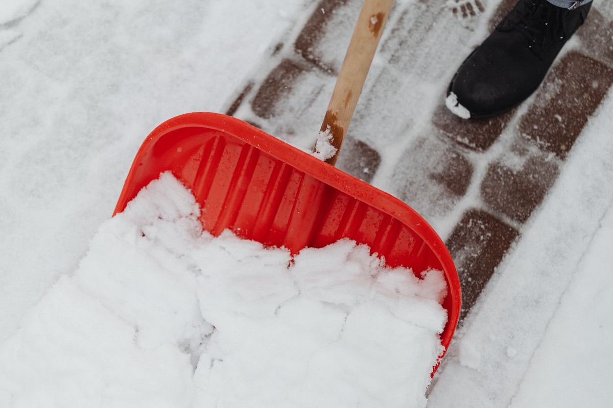 Gepflasterter Gehweg wird mit einer Schneeschaufel vom Schnee geräumt